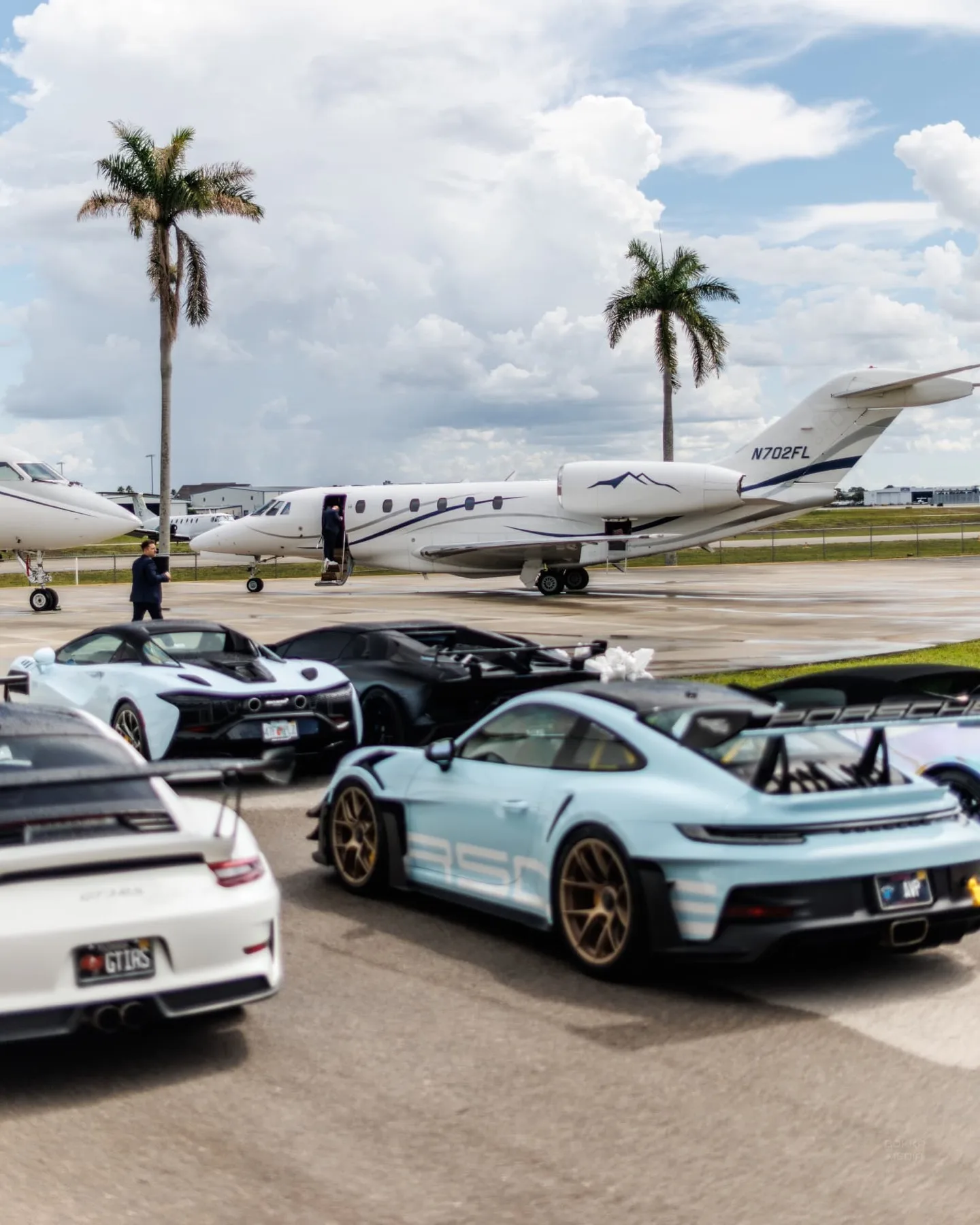 Supercars parked beside a private jet on a wet ramp in Fort Lauderdale