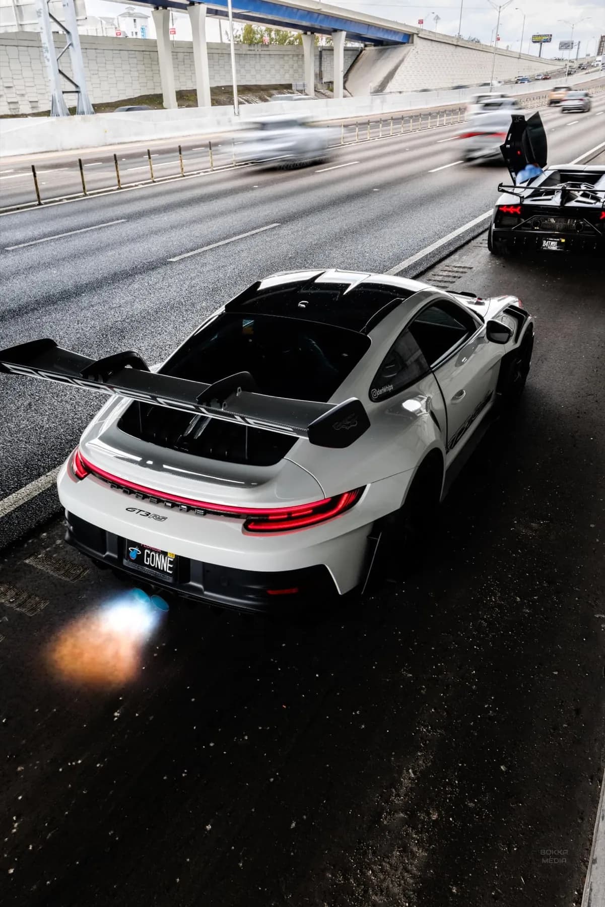 White Porsche GT3 RS shooting blue flames from its exhaust on a highway shoulder