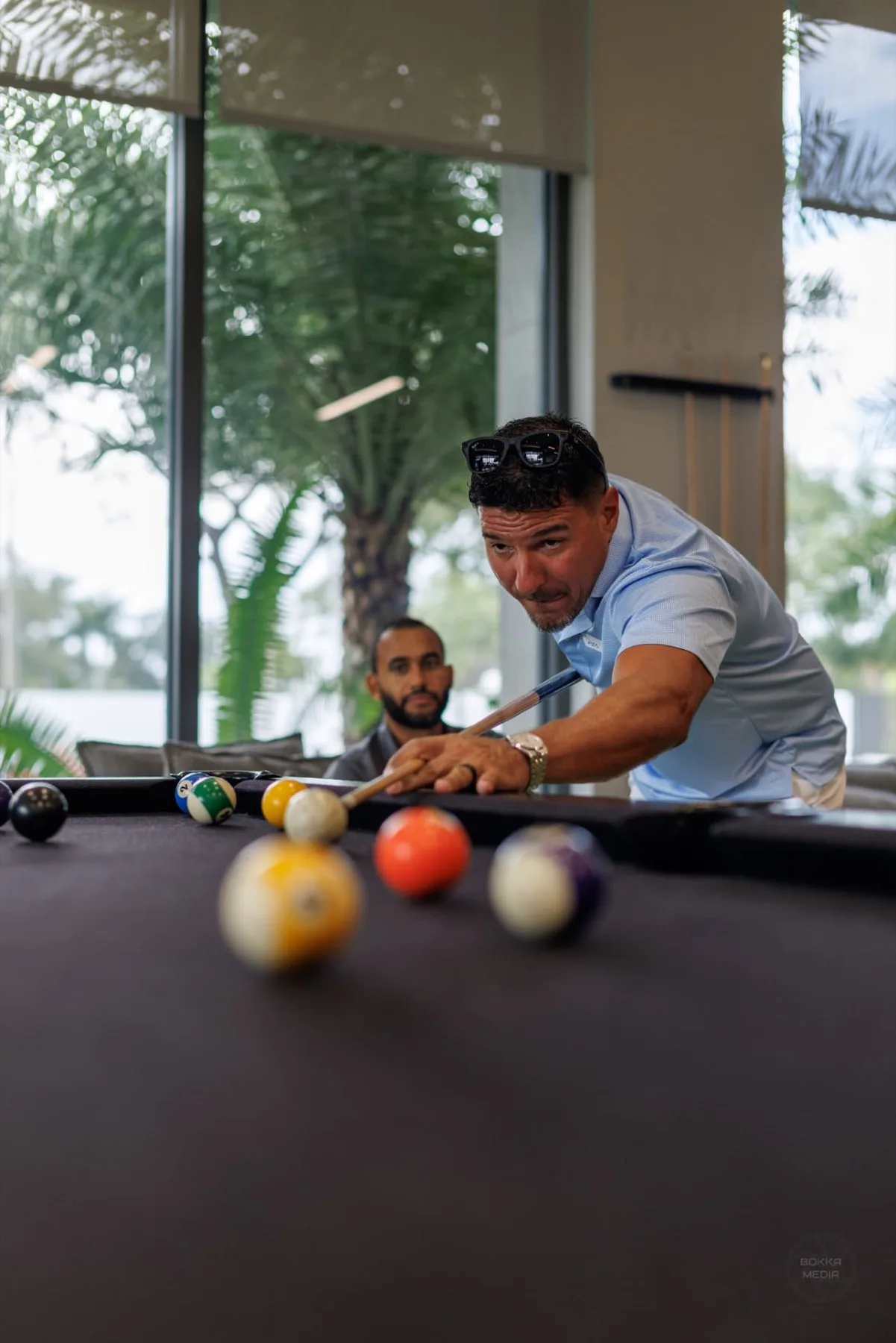 A guest lining up a shot while another watches from the lounge sofa
