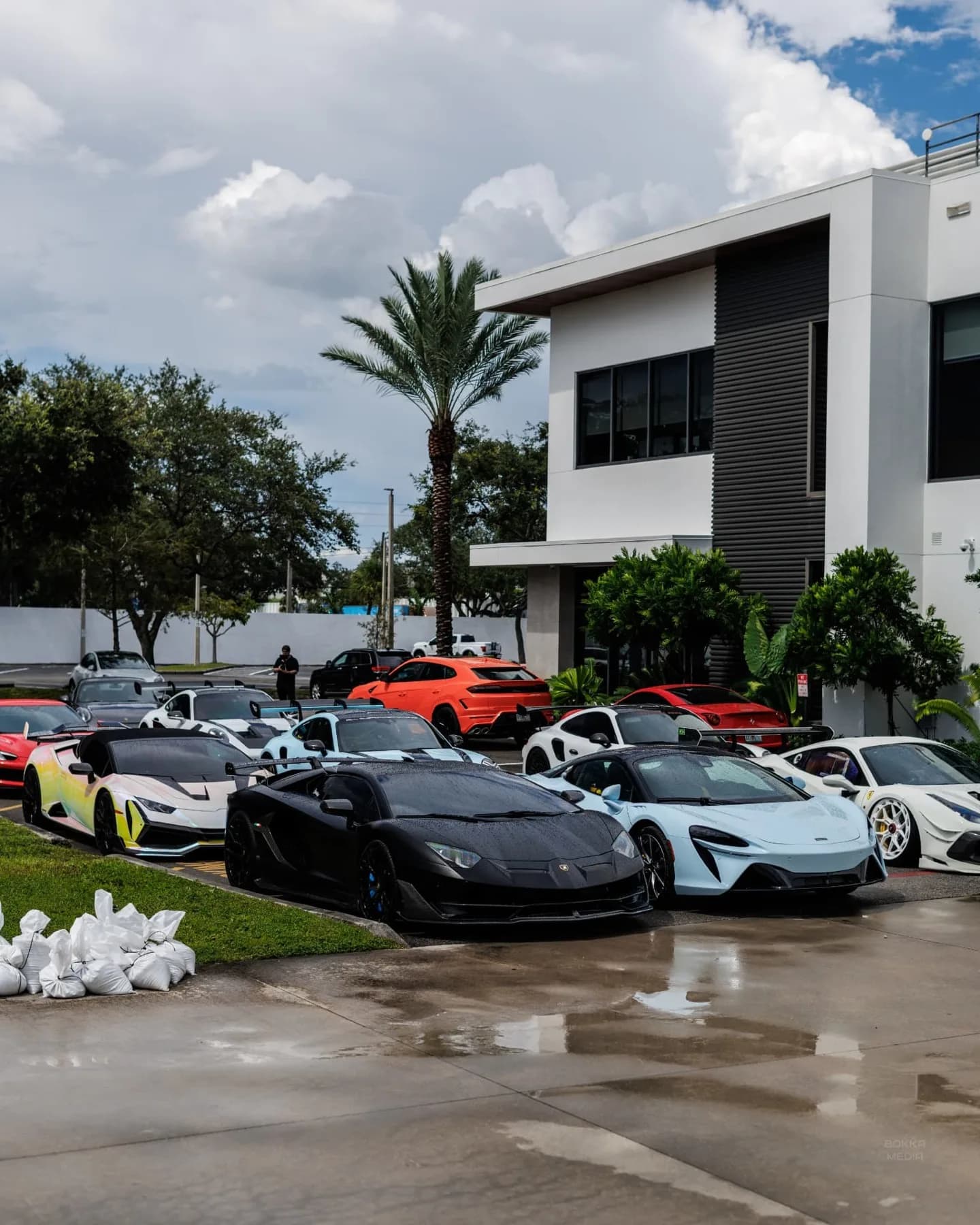 Supercar lineup parked in front of a modern white office building
