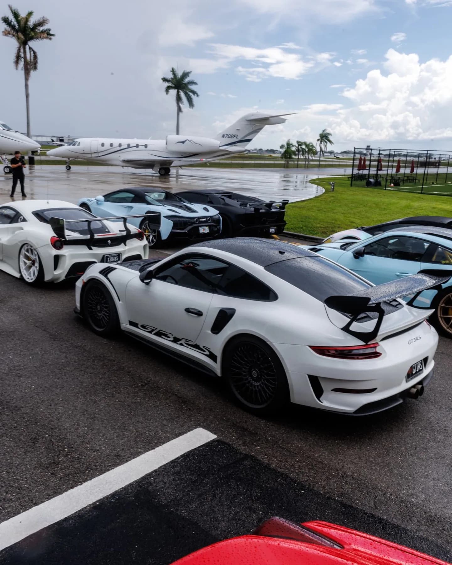 Row of supercars on the tarmac beside a private jet and palm trees