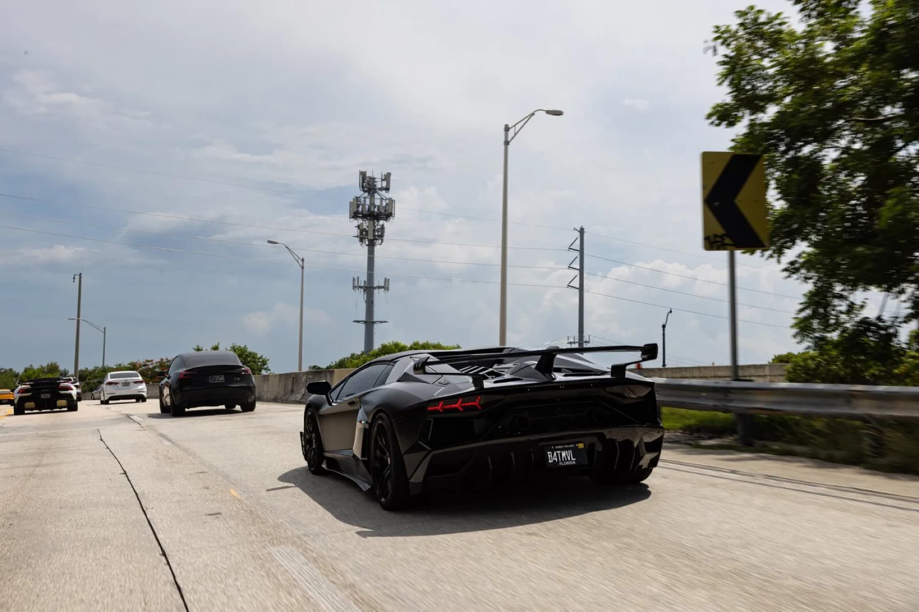 A matte black Lamborghini Aventador SVJ driving away along a Miami road at the end of the day.