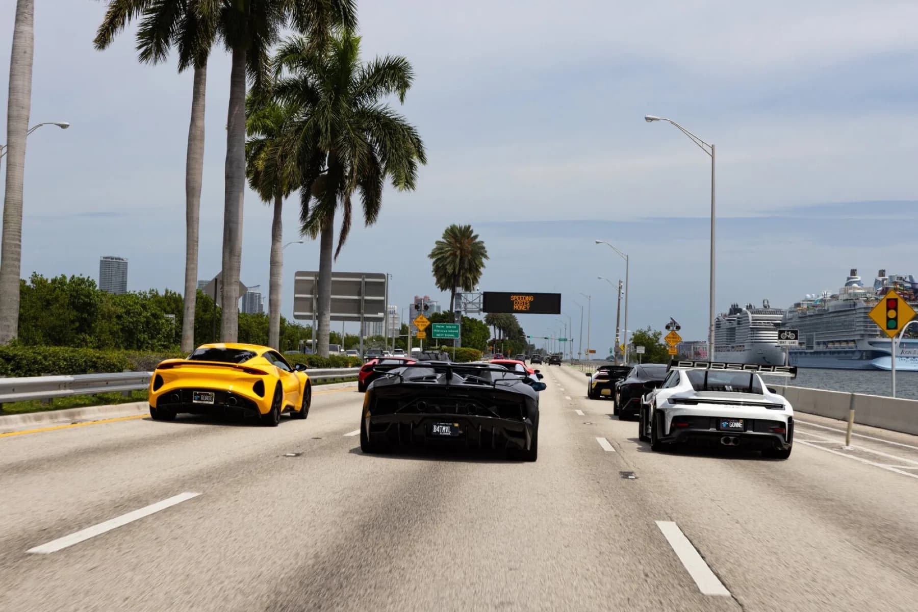 Eight supercars holding formation in a single line along a Miami causeway.