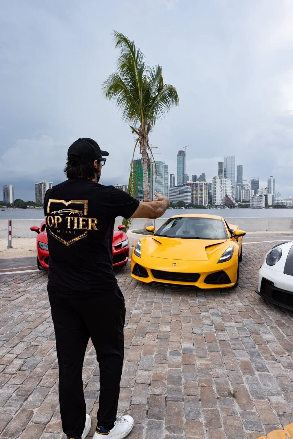 Dao, in a Top Tier Miami shirt, directing a yellow Lotus Emira into the last open spot in the lineup.