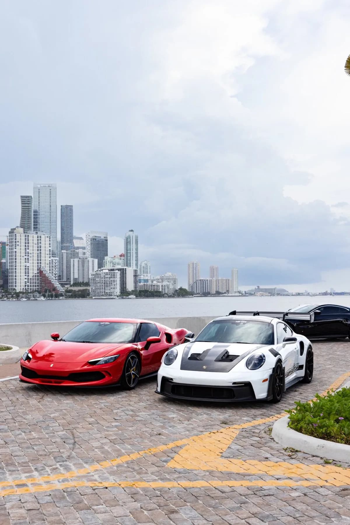 Samir's red Ferrari 296 and Dao's white Porsche 911 GT3 RS parked side by side with the Miami skyline behind them.